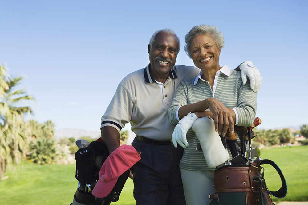 Older Couple with arms around each other smiling and leaning on their golf clubs