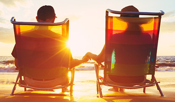 Retired couple sitting in beach chairs by the water watching the sunset